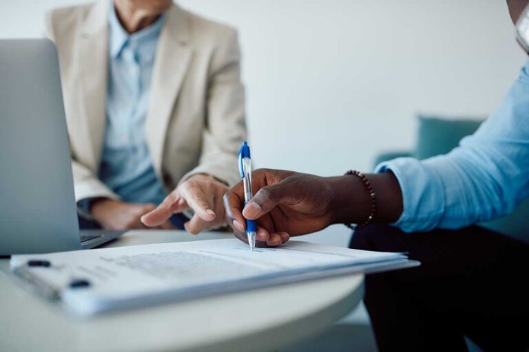 A person reviews an overdue insurance bill at a kitchen table with a pen and paperwork.