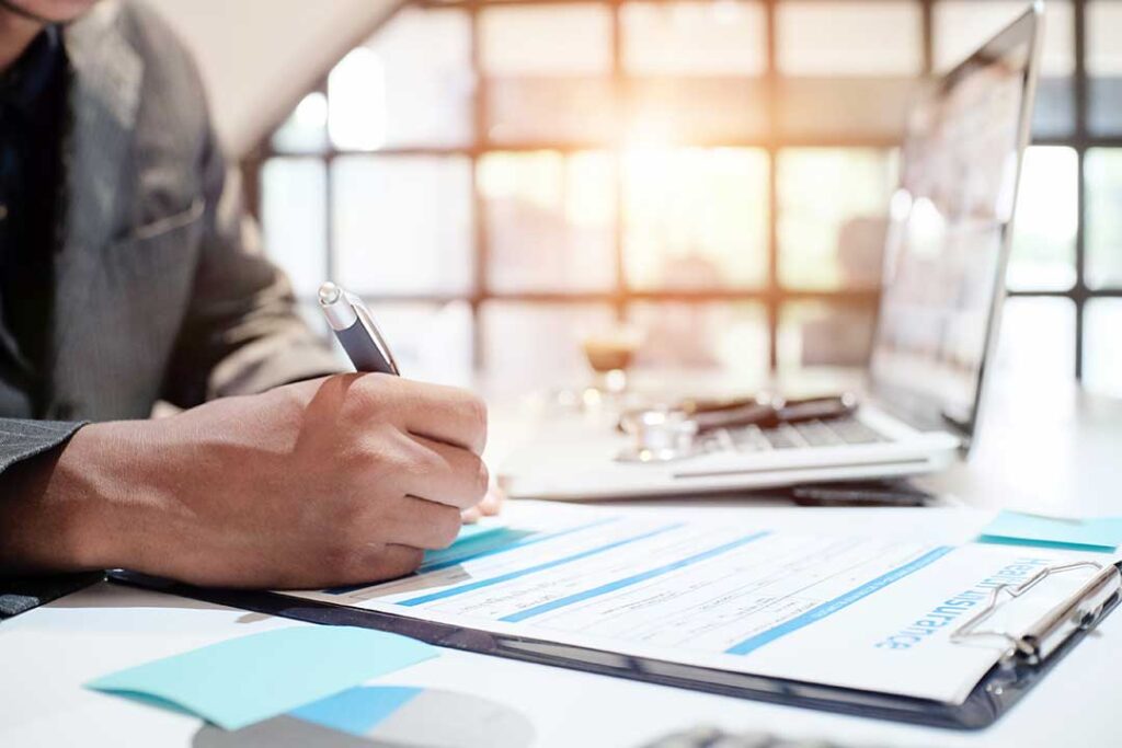 Parent and college student reviewing an insurance card and health plan papers at a kitchen table.