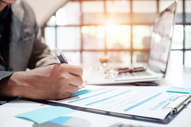 Parent and college student reviewing an insurance card and health plan papers at a kitchen table.