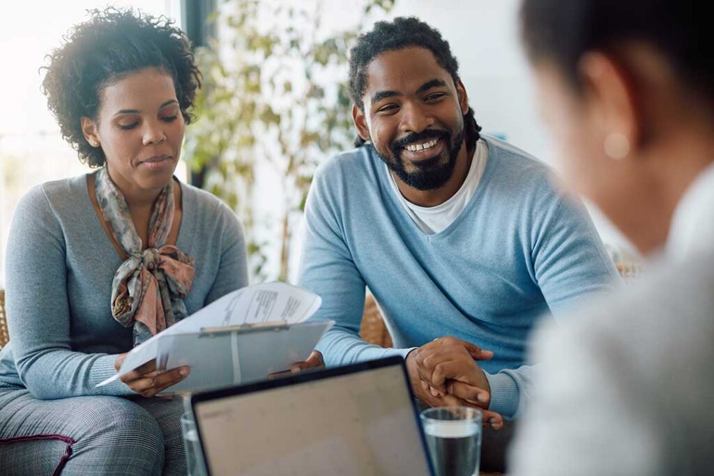 Parent organizing household papers at a kitchen table while children play nearby.