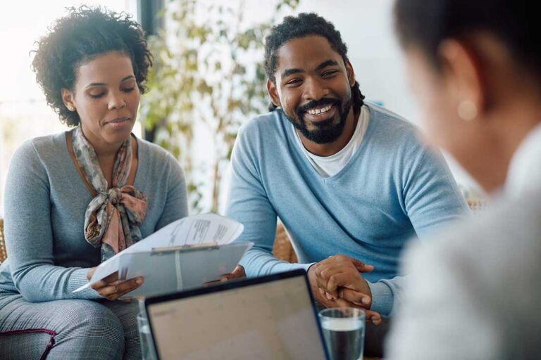 Parent organizing household papers at a kitchen table while children play nearby.